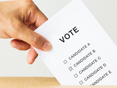 voting, civil rights and people concept - close up of male hand putting vote into ballot box on election